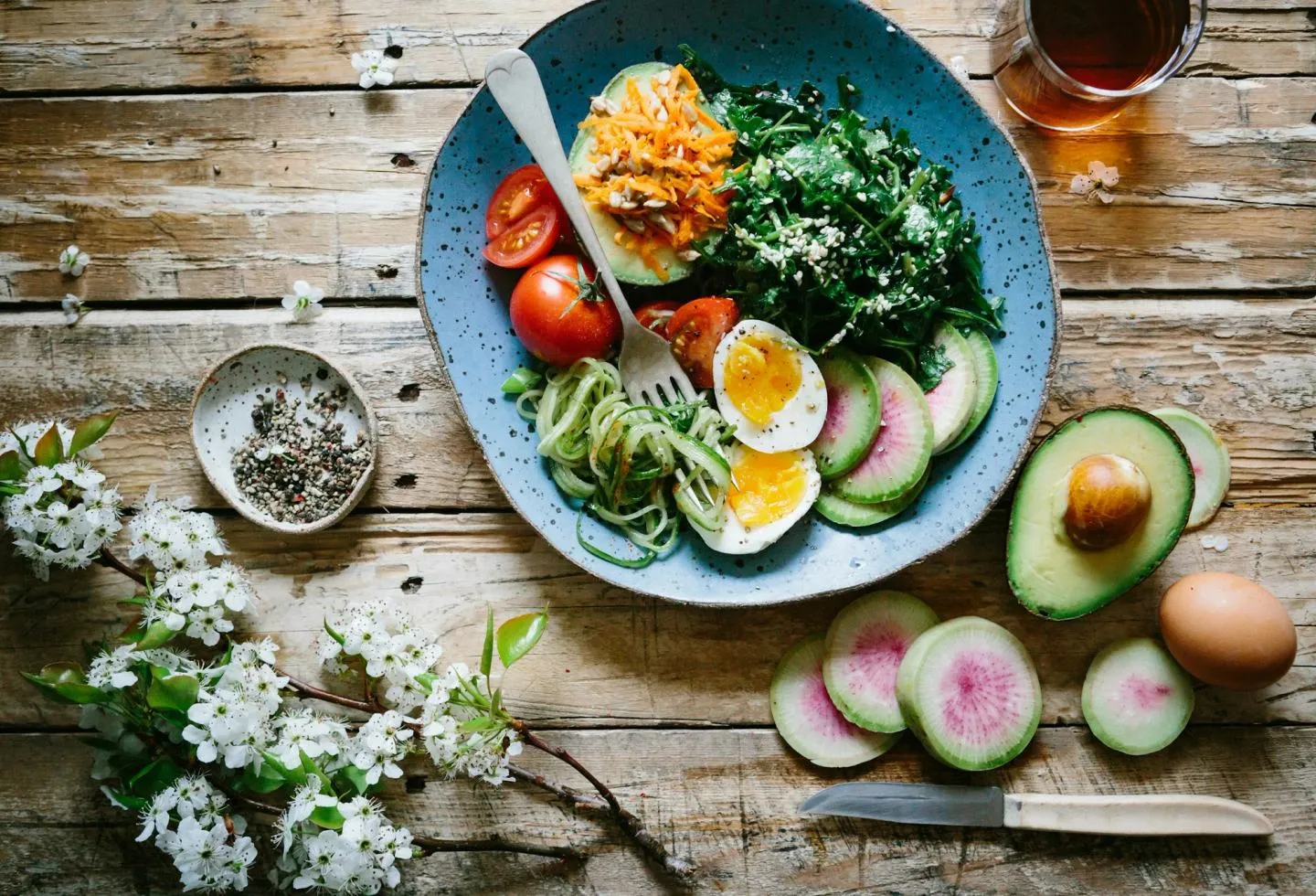 An overhead breakfast plate with a boiled egg, avocado, radish and salad greens on a wooden table