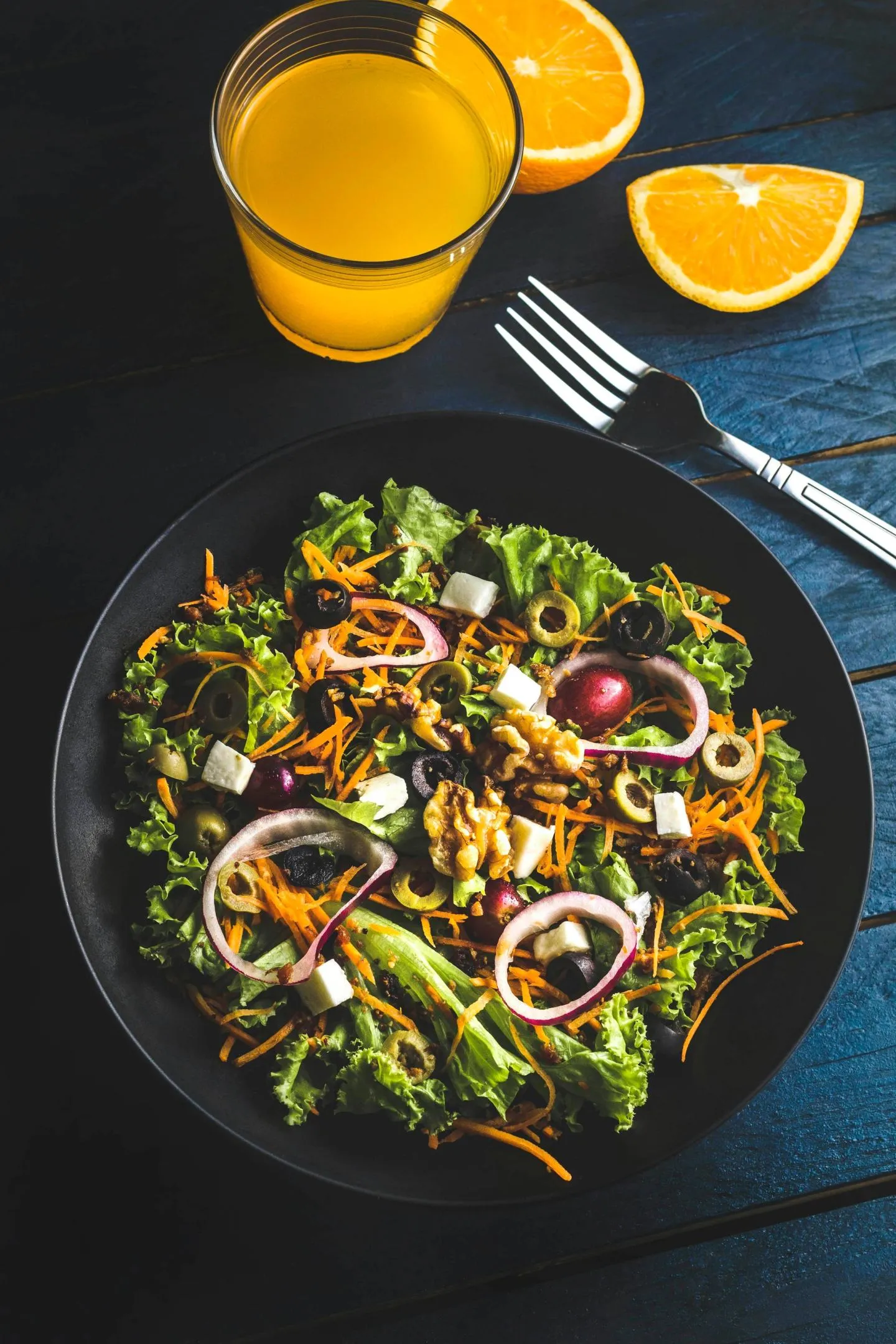A dark overhead composition of a salad bowl and a glass of orange juice on a black surface