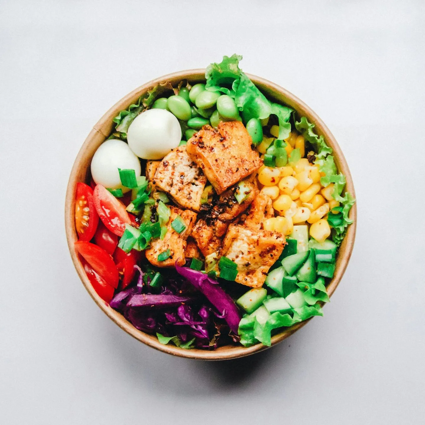 A grain bowl viewed from above with salmon, sweetcorn, tomato, cucumber and mixed greens