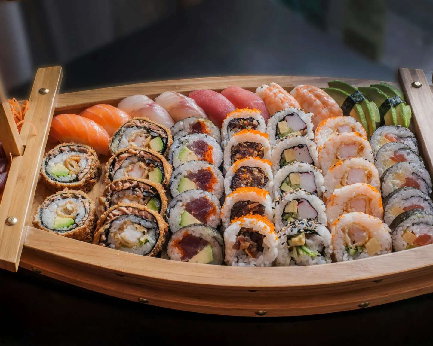 A long wooden boat platter arranged with dozens of pieces of sushi and maki rolls