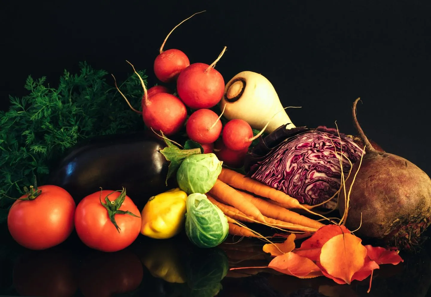 A dark still life of fresh vegetables including tomatoes, carrots, cabbage and peppers