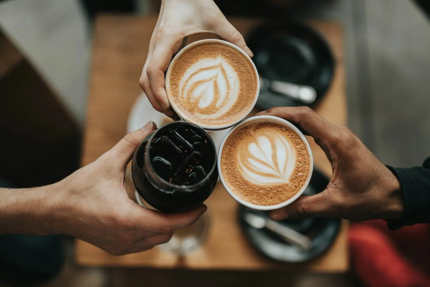 Two hands holding cappuccino cups with latte art over a wooden table