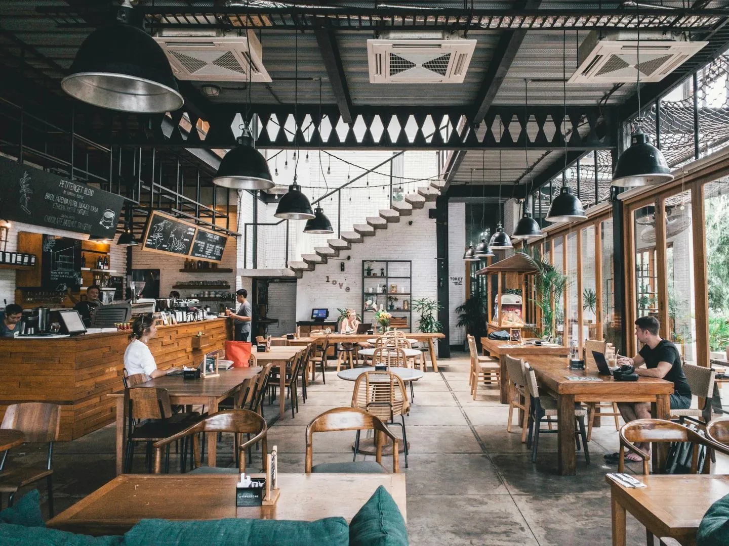 A busy industrial-style cafe interior with high ceilings, hanging lamps and diners at wooden tables