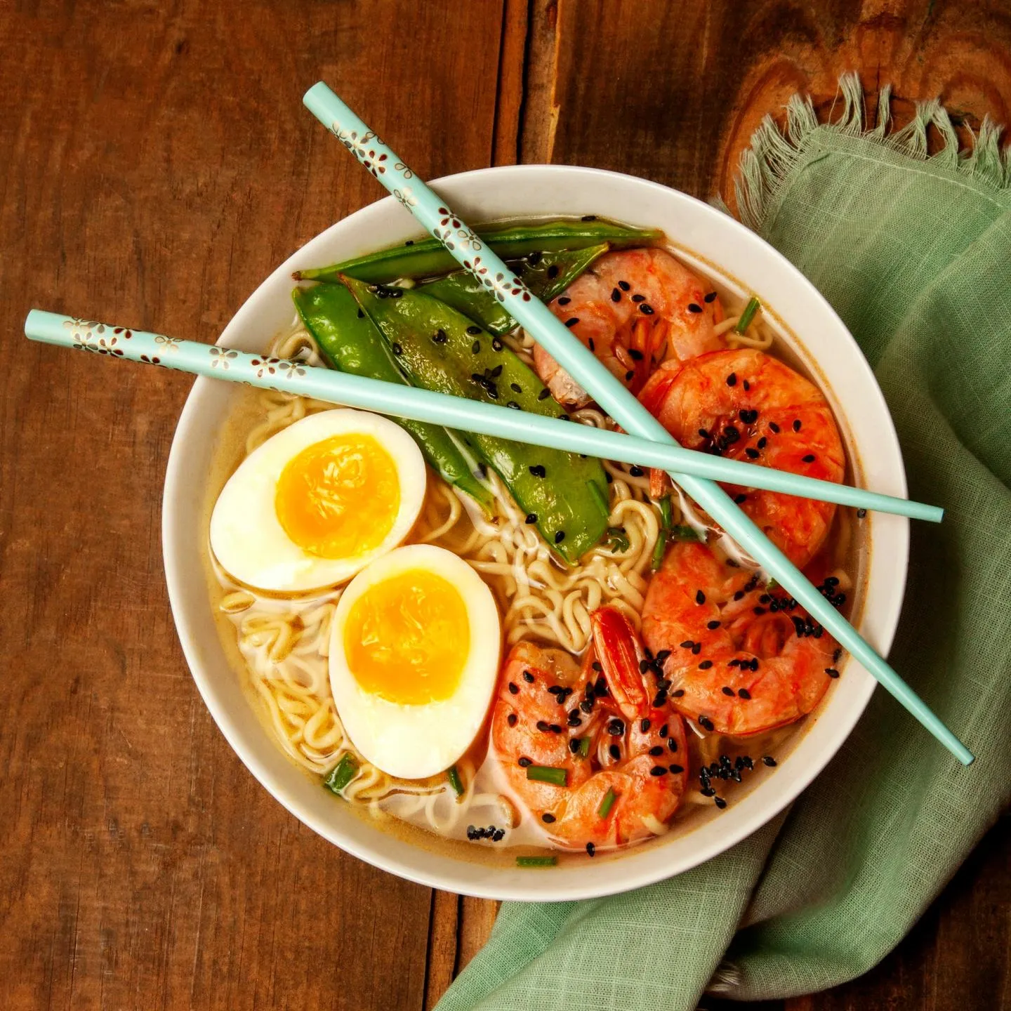 A bowl of ramen with a soft-boiled egg, sliced pork and greens, chopsticks resting across the rim